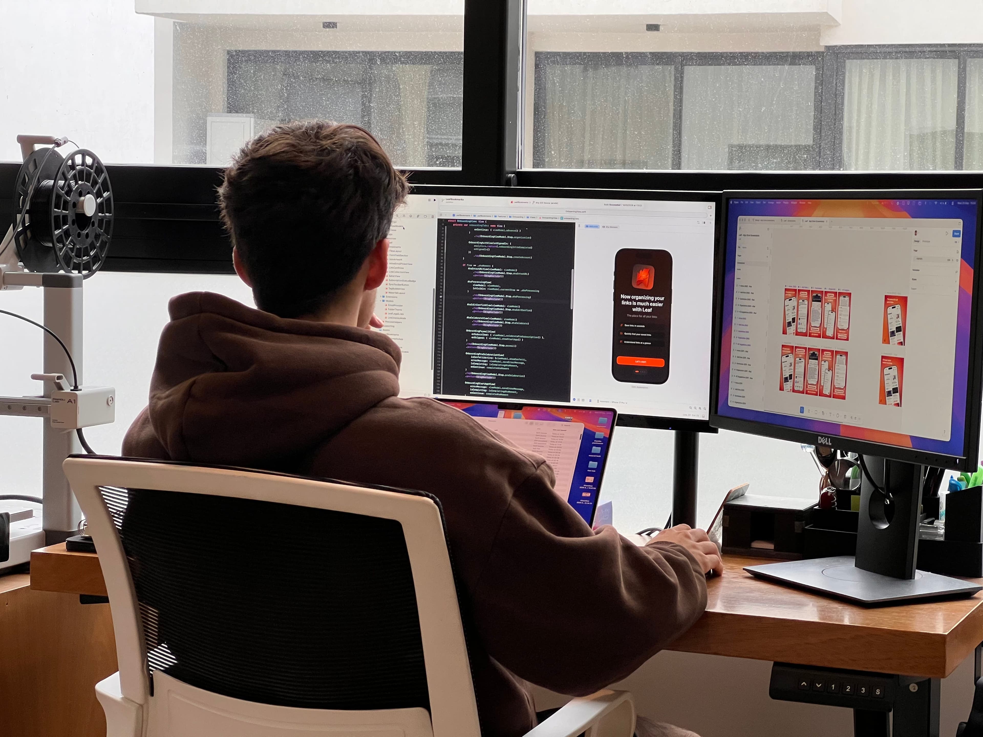 Tomás working in front of two monitors showing code and app designs